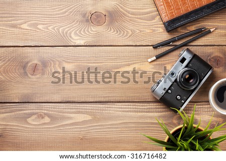 Camera and supplies on office wooden desk table. Top view with copy space