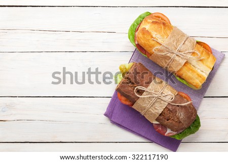 Two sandwiches with salad, ham, cheese and tomatoes on wooden table. Top view with copy space