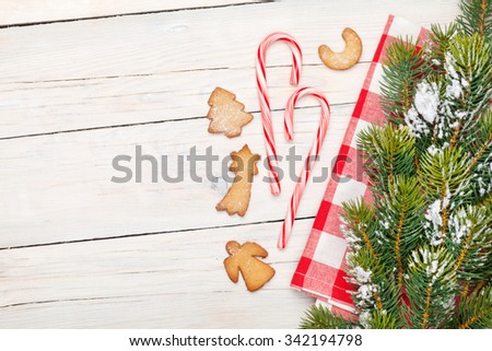 Christmas candy cane, gingerbread cookies and snow fir tree. View from above over white wooden table background