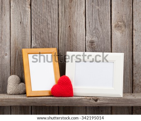 Blank photo frames and heart presents on shelf in front of wooden wall