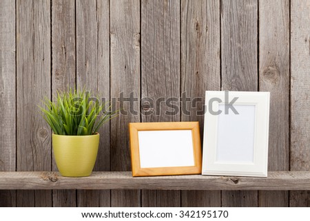 Blank photo frames and plant on shelf in front of wooden wall