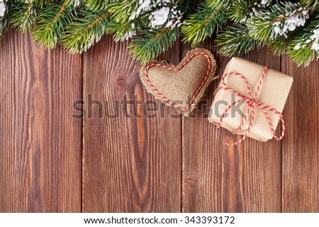 Christmas tree branch with snow, gift box and heart toy on wooden table. View with copy space