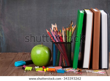 School and office supplies and apple on classroom table in front of blackboard. View with copy space