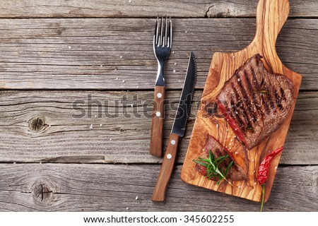 Grilled beef steak with rosemary, salt and pepper on wooden table. Top view with copy space