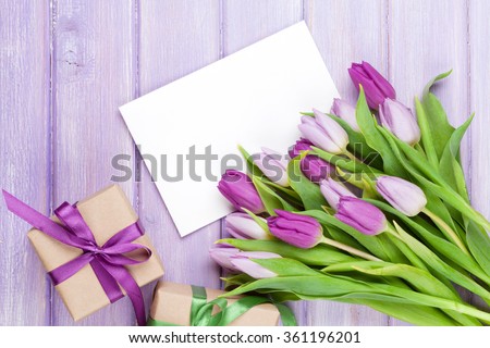 Purple tulip bouquet, blank greeting card and gift boxes. Top view over wooden table