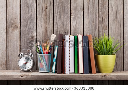 Wooden shelf with books and supplies in front of wooden wall. View with copy space