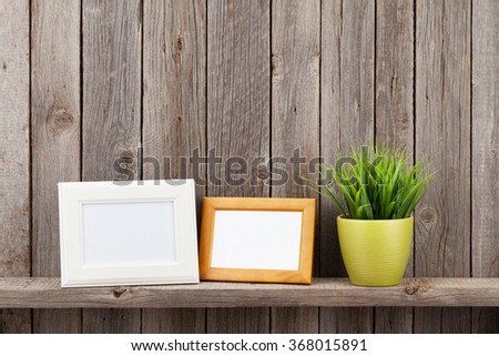 Blank photo frames and plant on shelf in front of wooden wall