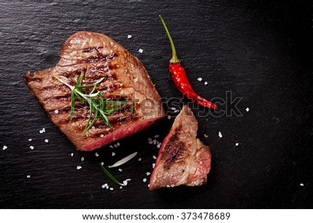 Grilled beef steak with rosemary, salt and pepper on black stone plate. Top view with copy space