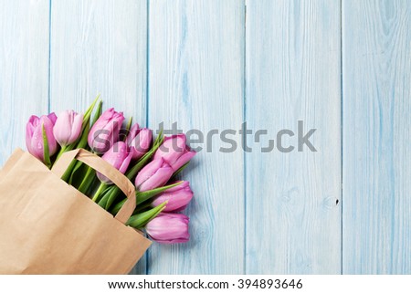 Fresh pink tulip flowers in paper bag on wooden table. Top view with copy space