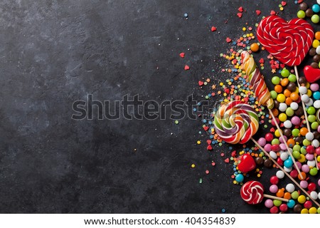 Colorful candies and lollipops over stone background. Top view with copy space