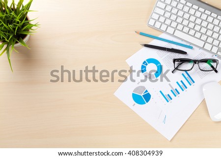 Office desk workplace with pc, charts and plant on wooden table. Top view with copy space