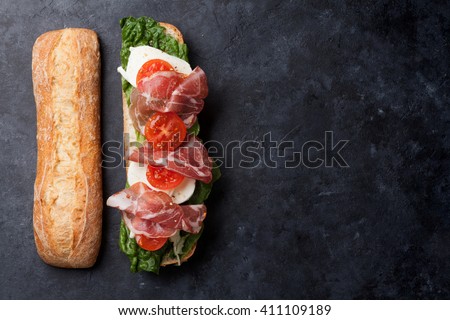 Ciabatta sandwich with romaine salad, prosciutto and mozzarella cheese over stone background. Top view with copy space