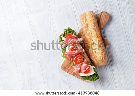 Ciabatta sandwich with romaine salad, prosciutto and mozzarella cheese over wooden background. Top view with copy space