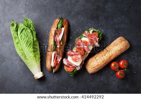 Ciabatta sandwich with romaine salad, prosciutto and mozzarella cheese over stone background. Sandwich ingredients. Top view
