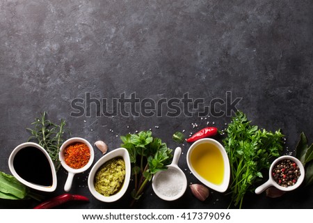 Herbs, condiments and spices on stone background. Olive oil and vinegar condiments. Mint, parsley and rosemary herbs. Salt, paprika and pepper spices. Top view with copy space