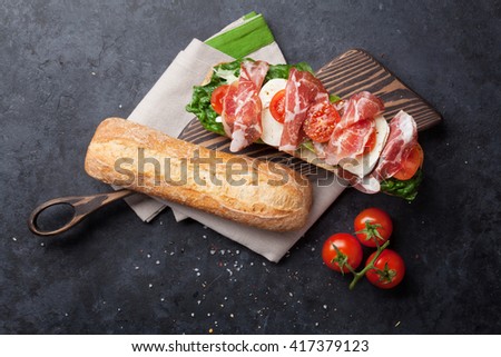 Ciabatta sandwich with romaine salad, prosciutto and mozzarella cheese over stone background. Sandwich cooking. Top view