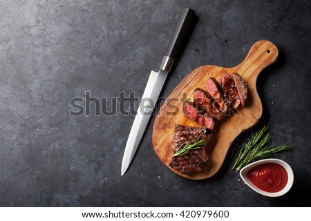 Grilled striploin sliced steak on cutting board over stone table. Top view with copy space