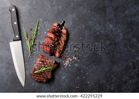 Grilled striploin sliced steak with salt and pepper and knife over stone table. Top view with copy space