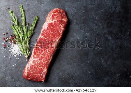 Raw striploin steak with rosemary, salt and pepper cooking over stone table. Top view with copy space
