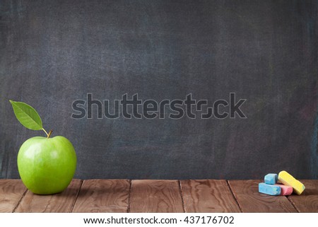 Apple fruit and chalks on classroom table in front of blackboard. View with copy space
