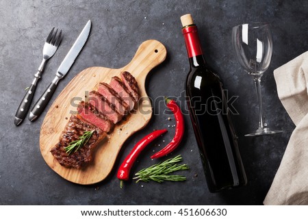 Grilled striploin sliced steak and red wine over stone table. Top view