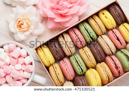 Colorful macaroons in a gift box and marshmallow in coffee cup on wooden table. Sweet macarons and flowers. Top view