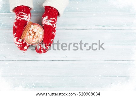 Female hands holding hot chocolate with marshmallow above wooden table. Top view with copy space