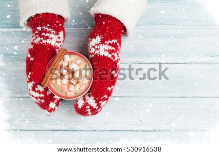 Female hands holding hot chocolate with marshmallow above wooden table. Top view with copy space