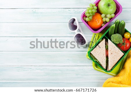 Lunch box with vegetables and sandwich on wooden background. Beach take away food box, towel and glasses. Top view with space for your text