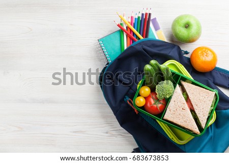 Lunch box with vegetables and sandwich on wooden table. Kids take away food box and school backpack. Top view with copy space