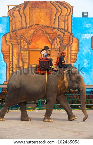 SURIN, ISAN, THAILAND - NOVEMBER 19, 2010: An elephant carries paying passengers past an oversized temple drawing at the annual Surin Elephant Roundup on November 19, 2010 in Surin, Thailand