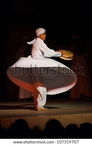 CAIRO, EGYPT - JULY 3: A Sufi dancer in white spins and beats a drum during a whirling dervish at an open air courtyard performance, a famous tourist attraction in Cairo, Egypt on July 3, 2010