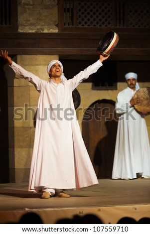 CAIRO, EGYPT - JULY 3: A Sufi dancer in white raises his arms after a whirling dervish at an open air courtyard performance, a famous tourist attraction in Cairo, Egypt on July 3, 2010