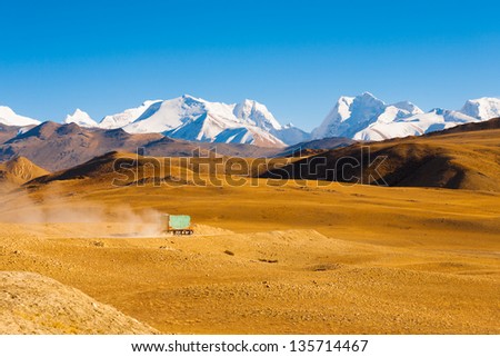 A truck drives through the barren landscape of the mountainous border between Tibet and Nepal as snowcapped himalayan mountain peaks poke through in the distance