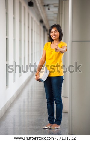 A cute smiling Asian student gives a thumbs up on a modern college campus.  20s female Asian Thai model of Chinese descent.