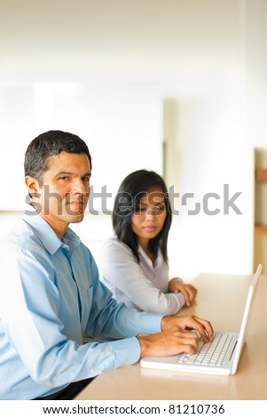 Hispanic male businessman types on a laptop during a one on one meeting with an attractive Asian businesswoman.