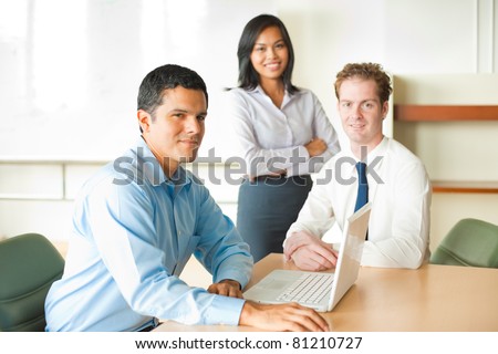 A latino businessman leads a diverse team of business people including an attractive Asian woman and caucasian male.