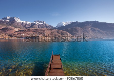 An old wooden pier faces the snow-capped mountains of the French alps on beautiful Lake Annecy.  Horizontal