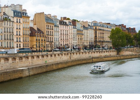 A tourist boat floats down the Seine river alongside beautifully typical Parisian architecture on a moody day in Paris, France.