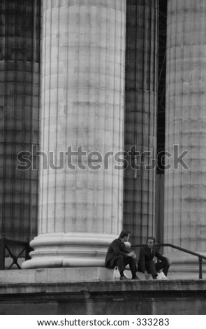 Low angle view of two businessmen sitting under columns of a building, Paris, France (black and white),