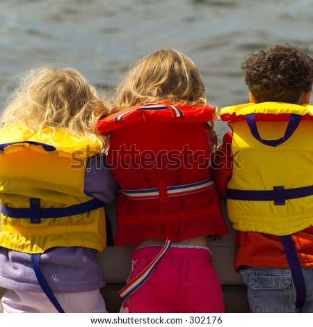 Rear view of three young children standing side by side wearing life jackets,