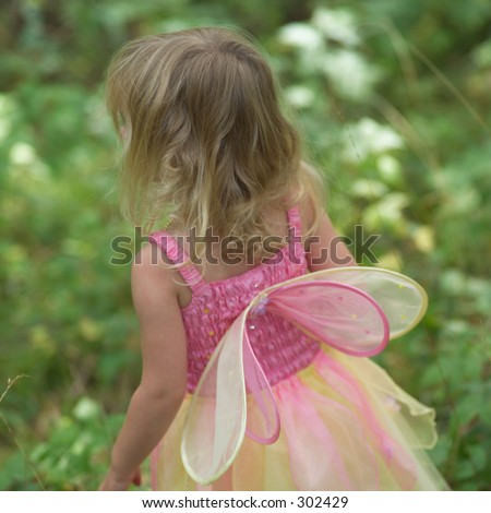 Rear view of a young girl in a fairy costume standing in a garden,