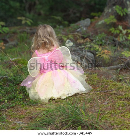 Rear view of a young girl in a fairy costume squatting in the grass,