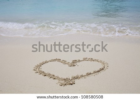 Heart symbol drawn in sand beach with blue ocean water