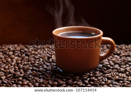 Brown cup of coffee with steam over a coffee beans