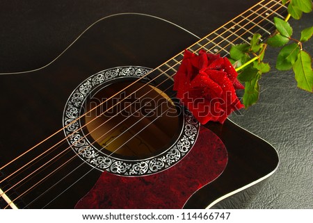 Acoustic black guitar and red rose against a textured background
