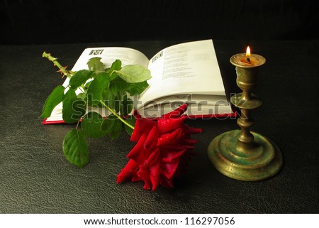 The open book, red rose and candle on a black background