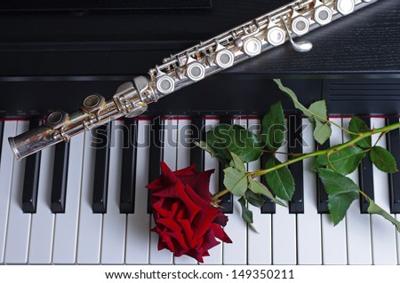 Piano keyboard, red rose and flute