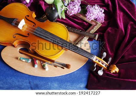 Still life with violin, art palette, brushes, bunch of lilac and drapery on the blue table-cloth