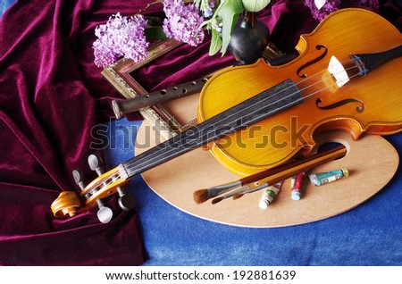 Still life with violin, art palette, brushes, bunch of lilac and drapery on the blue table-cloth
